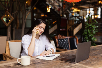 Young Caucasian business woman with long brunette hair working on laptop in cafe. College student using technology , online education, freelance 