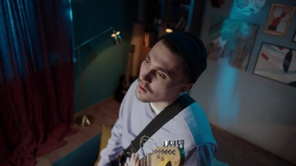 Young musician man standing on sofa singing and playing guitar happy and crazy, having fun, listening to music and dancing, social distance, band guitarist on lockdown, streaming concert. 