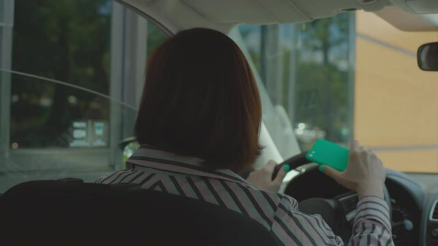 Young adult driver ordering fast food, paying bill with mobile phone and contactless terminal sitting in the car. Woman using NFC payment on her cellphone at fast food driving restaurant.