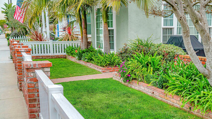 Pano Front yard of home with green lawn pathway wooden fence and red brick posts