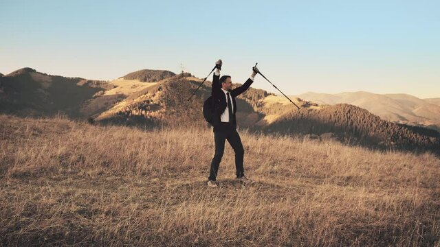 Sunny mountains, employee with trekking poles jumping, aerial. Goal achievement, active lifestyle. Dry grass and blue sky. Autumn landscape. Travel destinations. Hiking, vacation, holiday. Slow motion