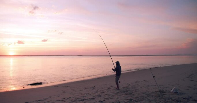 Silhouette of fisherman on sea coastline trying to cath a fish