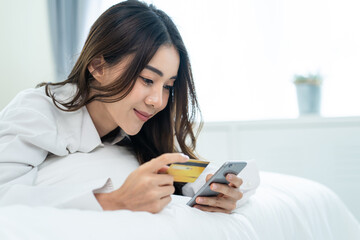 Asian attractive woman enjoy shopping online on bed at home in morning