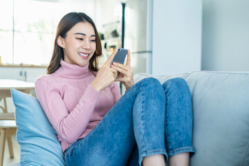 Obraz premium Asian beautiful woman sit on sofa and chat on mobile phone in house.
