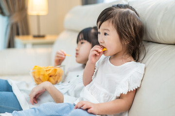 Obraz na płótnie Canvas Asian Hungry little girl sibling sisters Puts snack in mouth with hand
