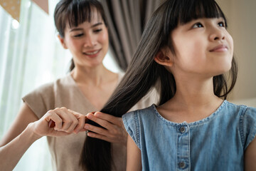 Asian mother combing little kid daughter's hair with hairbrush at home