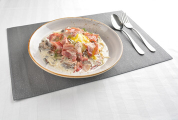 carbonara pasta with bacon, ham and half boiled egg in creamy cheese white sauce in white background western halal menu
