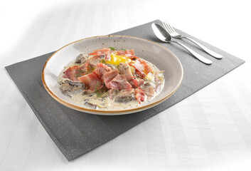 carbonara pasta with bacon, ham and half boiled egg in creamy cheese white sauce in white background western halal menu