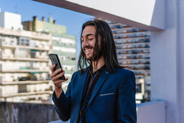 young hispanic latin long haired business man with his smart phone in his hand, chatting