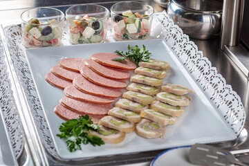 Slicing sausage, meat with herbs. Glasses with salad.