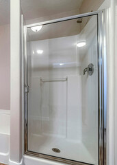 Vertical Shower stall and bathtub inside a clean bathroom with brown tiles on the floor
