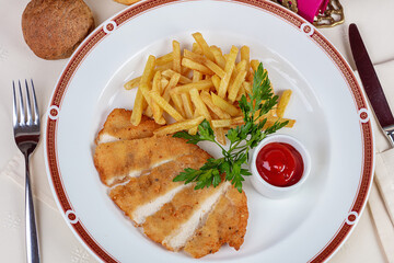 On a plate of French fries with sauce and herbs, chopped chicken breast in breadcrumbs.