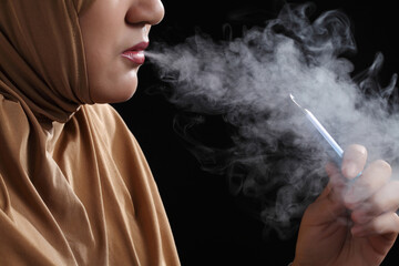 Close up young muslim woman smoking e-cigarette on black background