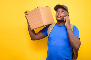 An African dispatch man with back pack, making a call, carrying boxes and wearing a face cap