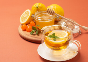 Ginger tea with mint and lemon. Healthy and hot drink. Liquid honey in honey-jar. Crystal cup on bright background. Selective focus.