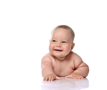 Happy laughing infant child baby girl kid in diaper is lying on her tummy holding arm outstretched, slapping on floor isolated on a white background
