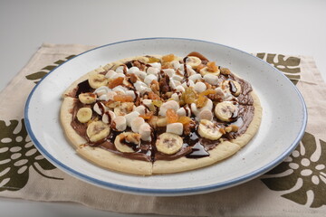 baked chocolate banana pizza with marshmallow and dry grape fruit dessert for kids in white background western halal menu