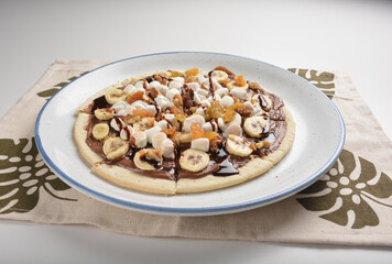 baked chocolate banana pizza with marshmallow and dry grape fruit dessert for kids in white background western halal menu