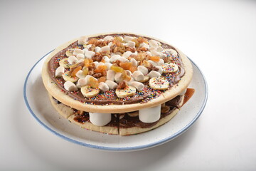 baked chocolate banana pizza with marshmallow and dry grape fruit dessert for kids in white background western halal menu