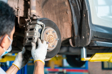 car mechanic examining car wheel brake disc and shoes of lifted automobile at auto repair service center - obrazy, fototapety, plakaty