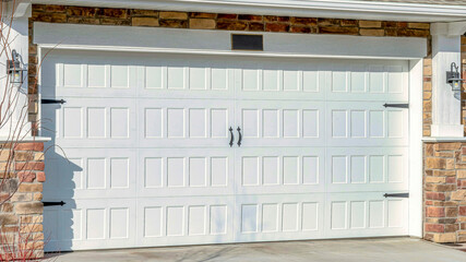 Pano Home with driveway leading to hinged white garage door against stone brick wall