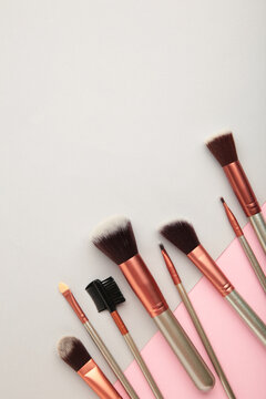 Various makeup brushes on grey and pink background with copy space. Vertical photo