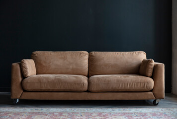 Comfortable sofa with pillows in the interior of a spacious living room, real photo with copy space on an empty black wall