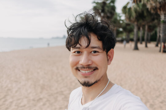 Happy Asian man take selfie with palm tree on the beach. Summer travel concept.