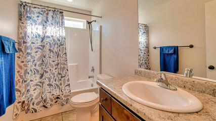 Pano Warm toned single sink vanity adjacent to toilet and bathtub with curtain