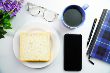Top View of Breakfast Concept White Bread on plate with smartphone flower and a cup of coffee on white background