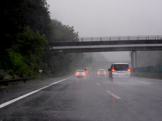 雨の高速道路でハザードを点滅させて渋滞を伝える車