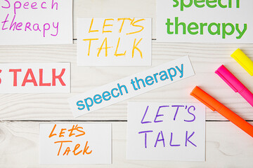 Paper pieces with text LET'S TALK and SPEECH THERAPY on white wooden background