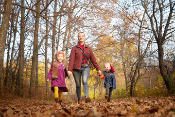 Two young little girl and his mother with blonde hair in an autumn park on a yellow and orange leaf background. Family walking in forest