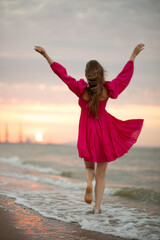 Young girl in a pink summer dress walks on the sea coast at sunrise. Blurred photo. Out of focus.