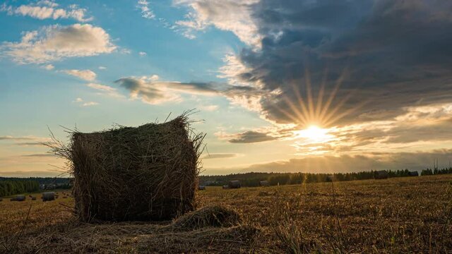 4K UHD flat hill meadow timelapse at the summer sunset time. Wild nature and rural haystacks on grass field. Sun rays and green trees. Motorised dolly slider