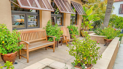 Pano Relaxing patio of house with wooden chair and bench against windows with awning - obrazy, fototapety, plakaty
