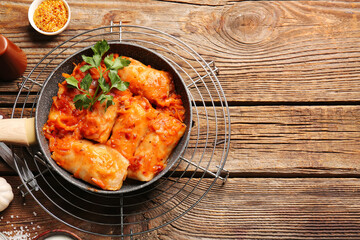 Frying pan with tasty stuffed cabbage rolls on wooden background