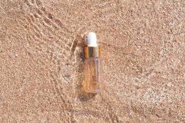 luxury face serum bottle on a beach sand with sea wave glare