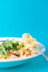 Traditional Italian pasta with clams and ruccola served in a white plate over blue background.