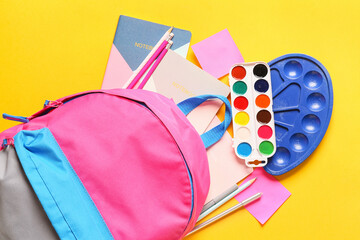 School backpack with stationery on color background