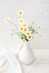 Vase with beautiful chamomile flowers on light wooden background