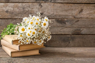 Bouquet of beautiful chamomile flowers and books on wooden background