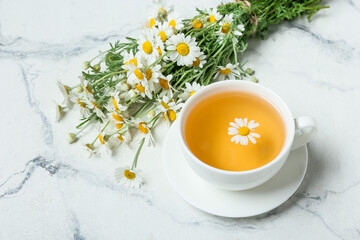 Cup of tea and bouquet of beautiful chamomile flowers on light background