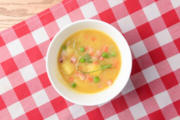 Traditional fresh pea soup in the white bowl over red plaid tablecloth.