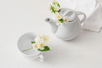 Composition with teapot, cup and beautiful jasmine flowers on light background
