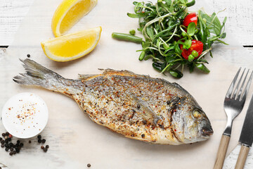 Fried dorado and salad on white wooden background