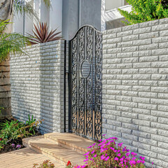 Square Pathway along wrought iron gate and brick fence at the entrance of modern home