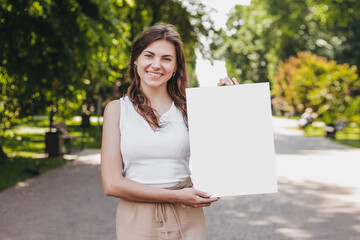 Happy caucasian young brunette woman holding a poster in her hands and smiling on the background of...