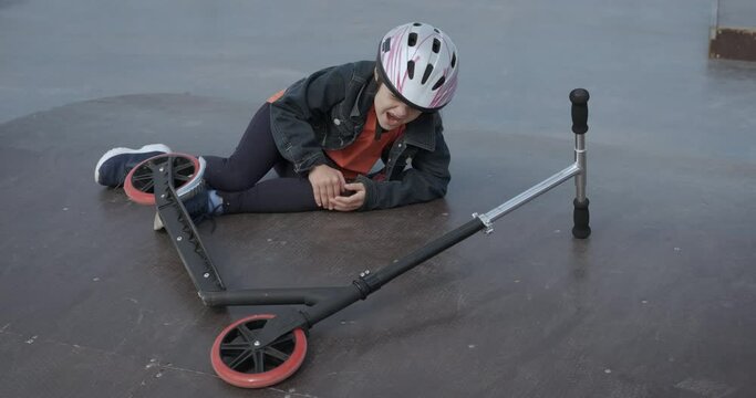 Sport child accident. A sad child fell dowm from her scooter on the playground.