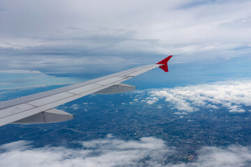 A shot through a window of an airplane shows the wings and the view below, with a number of clouds partially obscuring the view below.